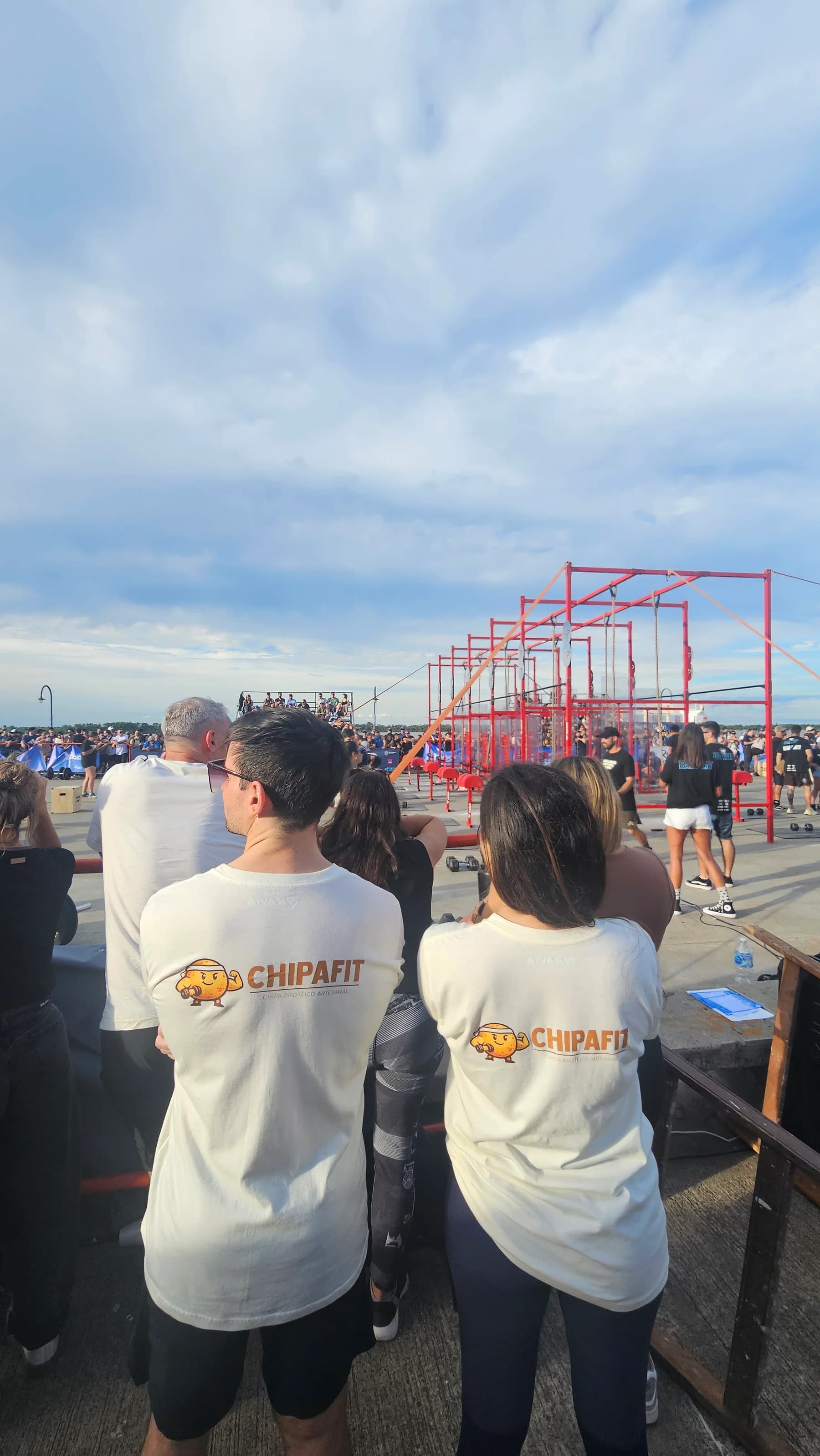 Dos personas con remeras de Chipa Fit miran la competencia desde el público